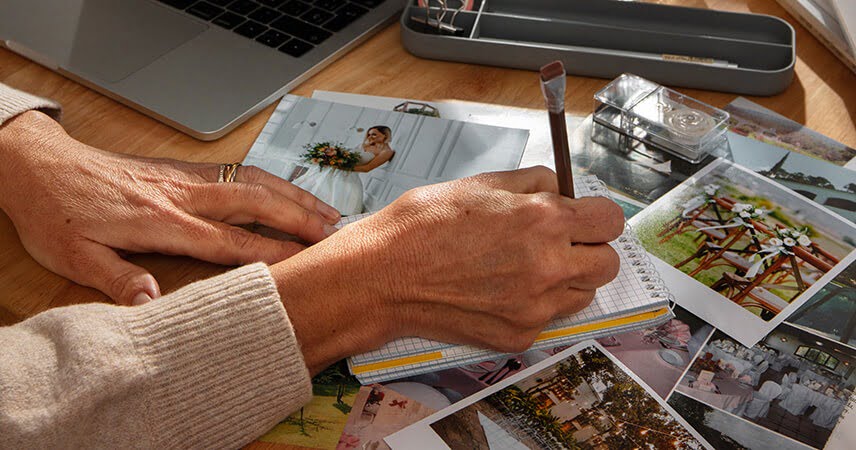 Een persoon met een lichte huid schrijft in een notitieboekje op een houten bureau. Diverse foto’s, waaronder één van een bruid, liggen verspreid. Er zijn een laptop, een etui en wat kantoorbenodigdheden in de buurt. De scène weerspiegelt de creativiteit en organisatie die vaak bij een brandingbureau te vinden is. Een persoon met een lichte huid schrijft in een notitieboekje op een houten bureau. Diverse foto's, waaronder één van een bruid, liggen verspreid. Er zijn een laptop, een etui en wat kantoorbenodigdheden in de buurt. De scène weerspiegelt de creativiteit en organisatie die vaak bij een brandingbureau te vinden is.